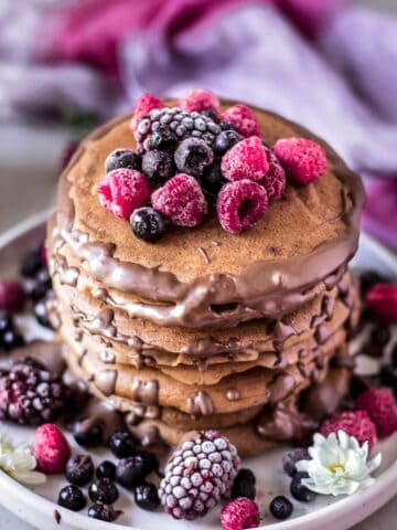 A stack of chocolate banana pancakes decorated with berries and chocolate sauce