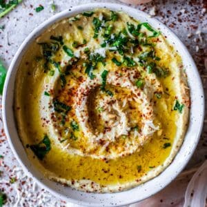 A bowl of low FODMAP hummus drizzled with olive oil and sprinkled with chilli flakes and parsley