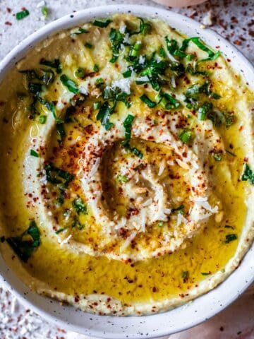 A bowl of low FODMAP hummus drizzled with olive oil and sprinkled with chilli flakes and parsley
