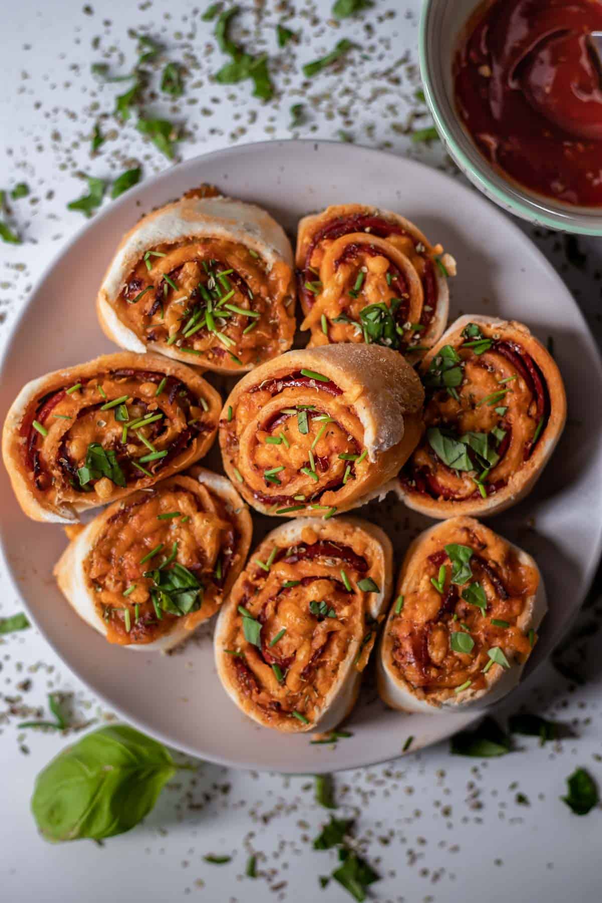 Gluten-free pizza rolls on a plate with tomato sauce on the side.