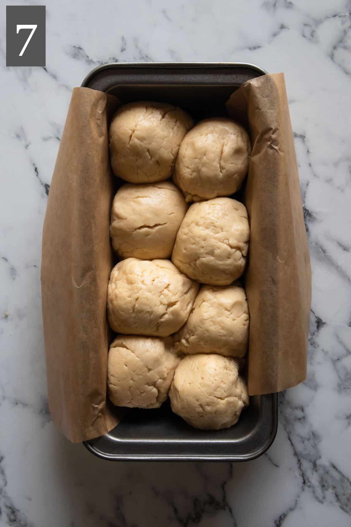 The dough balls arranged in a loaf tin in a zip zag manner.
