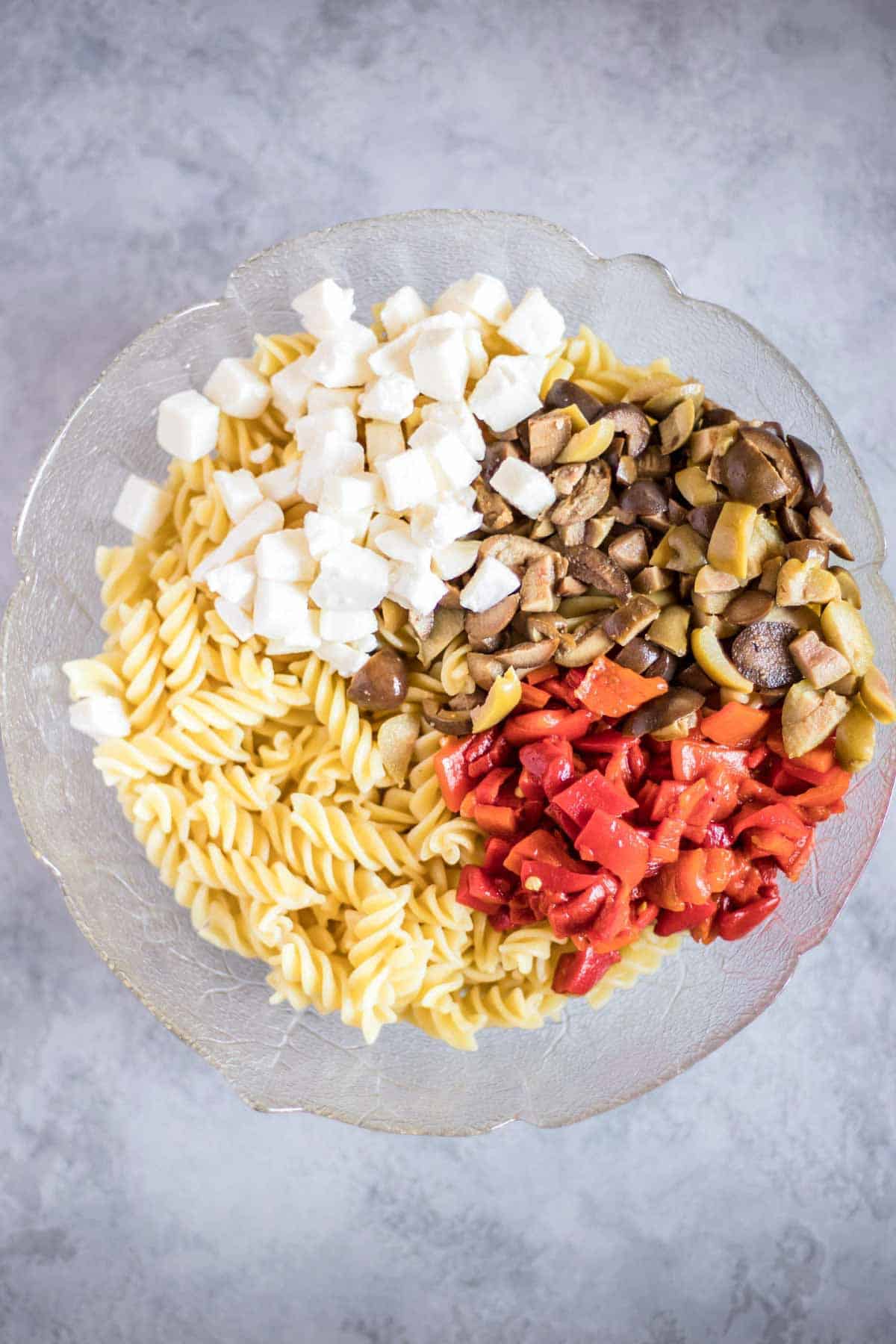 A salad bowl with gluten-free rotini pasta, mozzarella balls, olives and roasted red pepper.