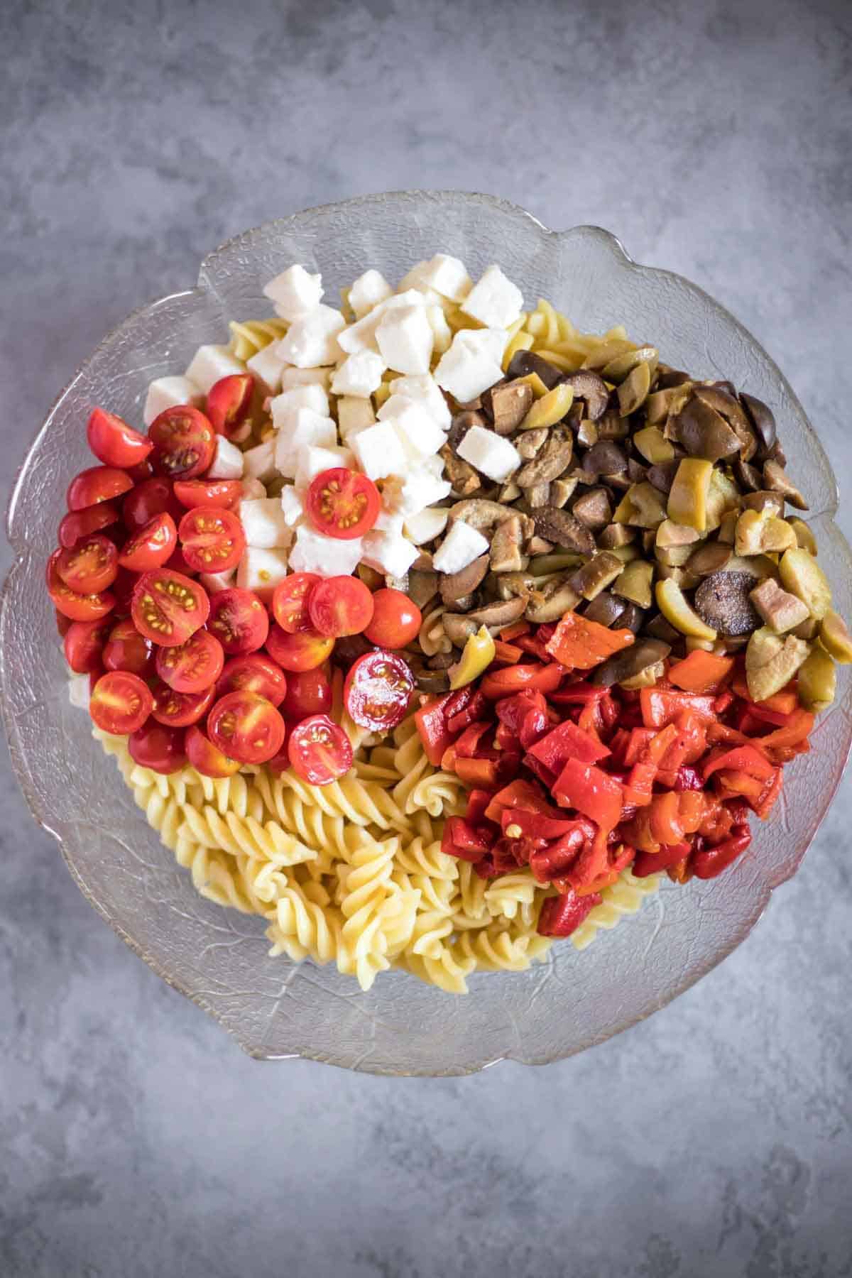 A salad bowl with gluten-free rotini pasta, cherry tomatoes, mozzarella balls, olives and roasted red pepper.