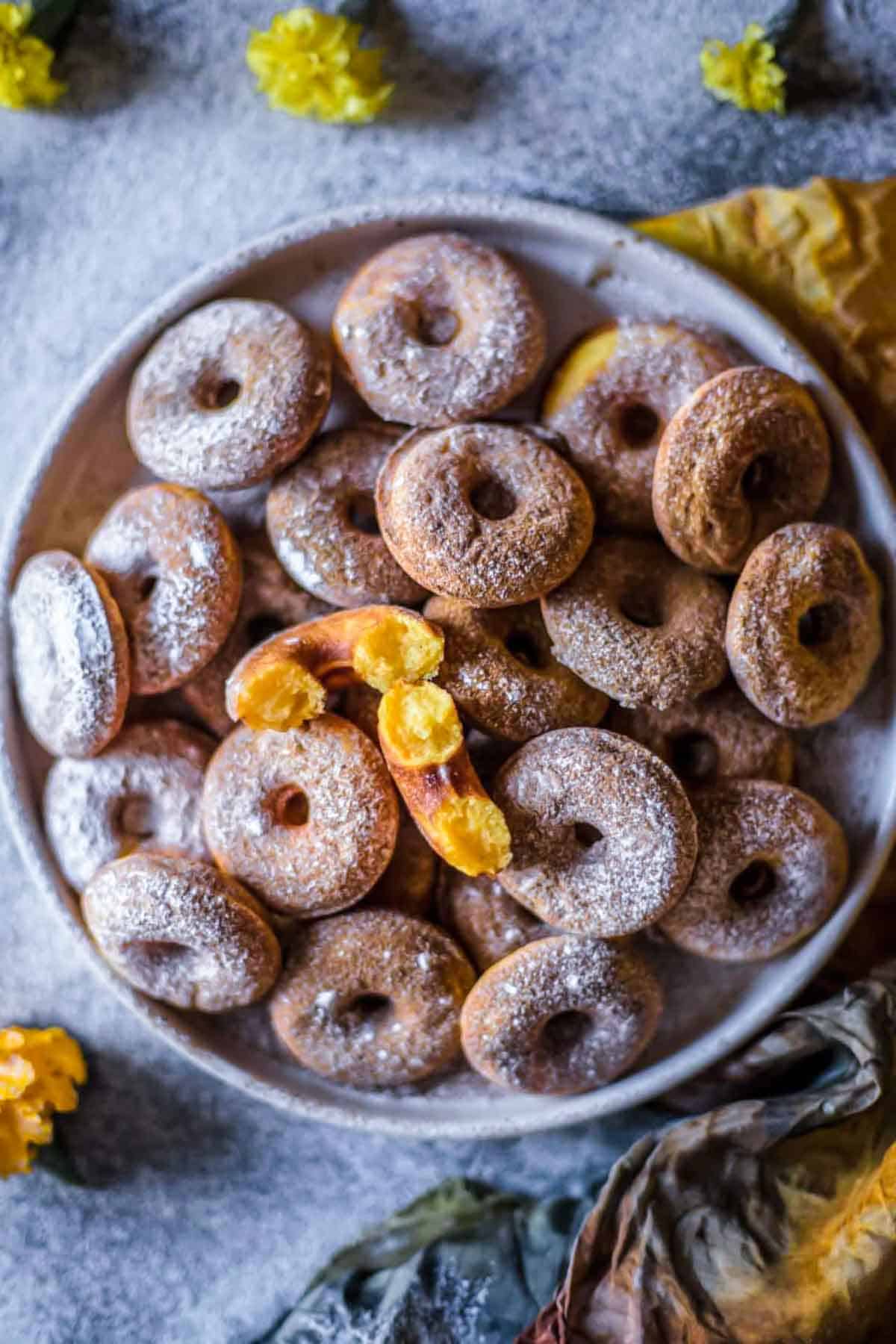 Gluten-free pumpkin donuts on a plate with one donut broken in half to show the texture.