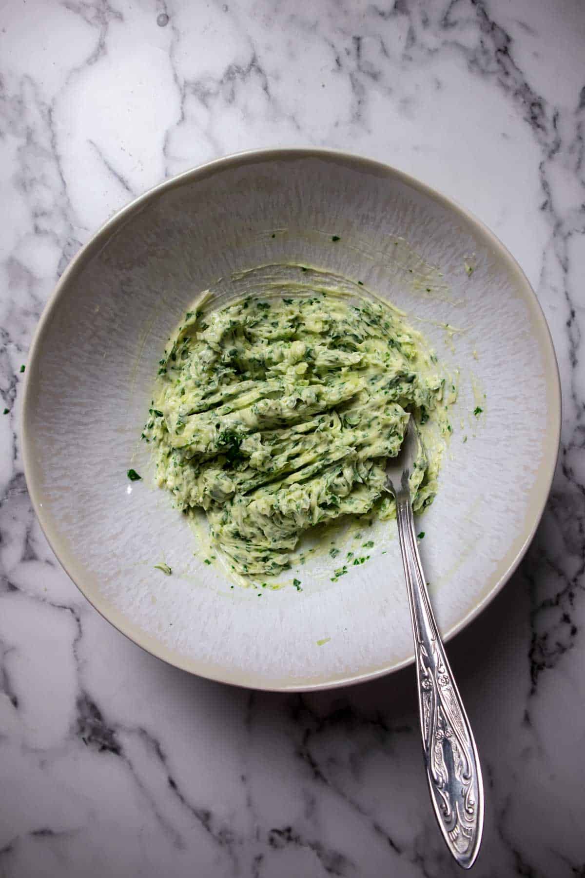 Making garlic butter by mixing butter, garlic and parsley.