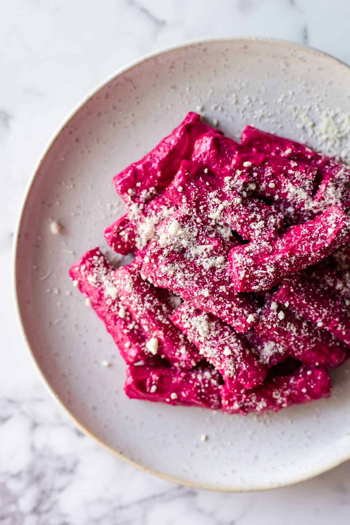 A plate of pasta with creamy beet sauce topped with parmesan