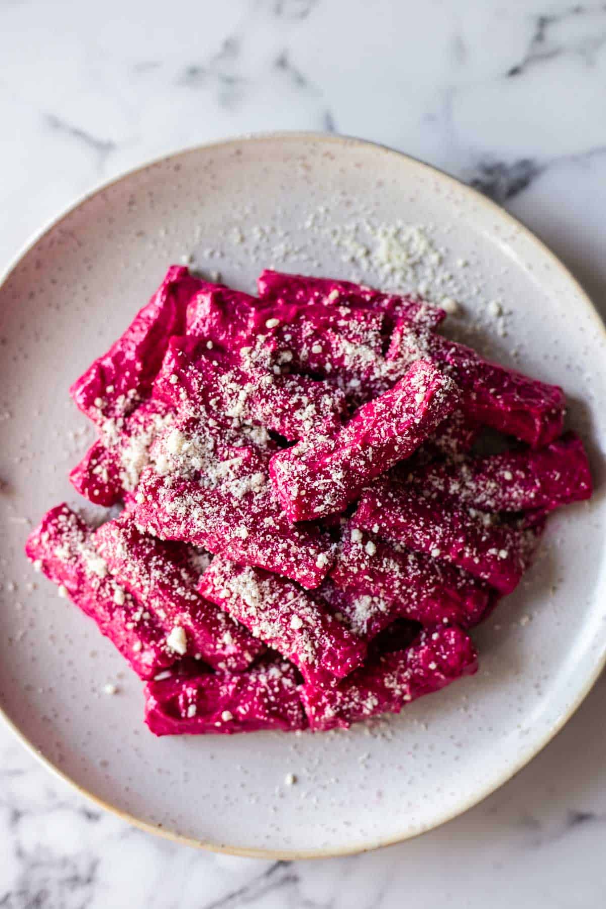 Pasta with beet sauce served on a plate with parmesan cheese