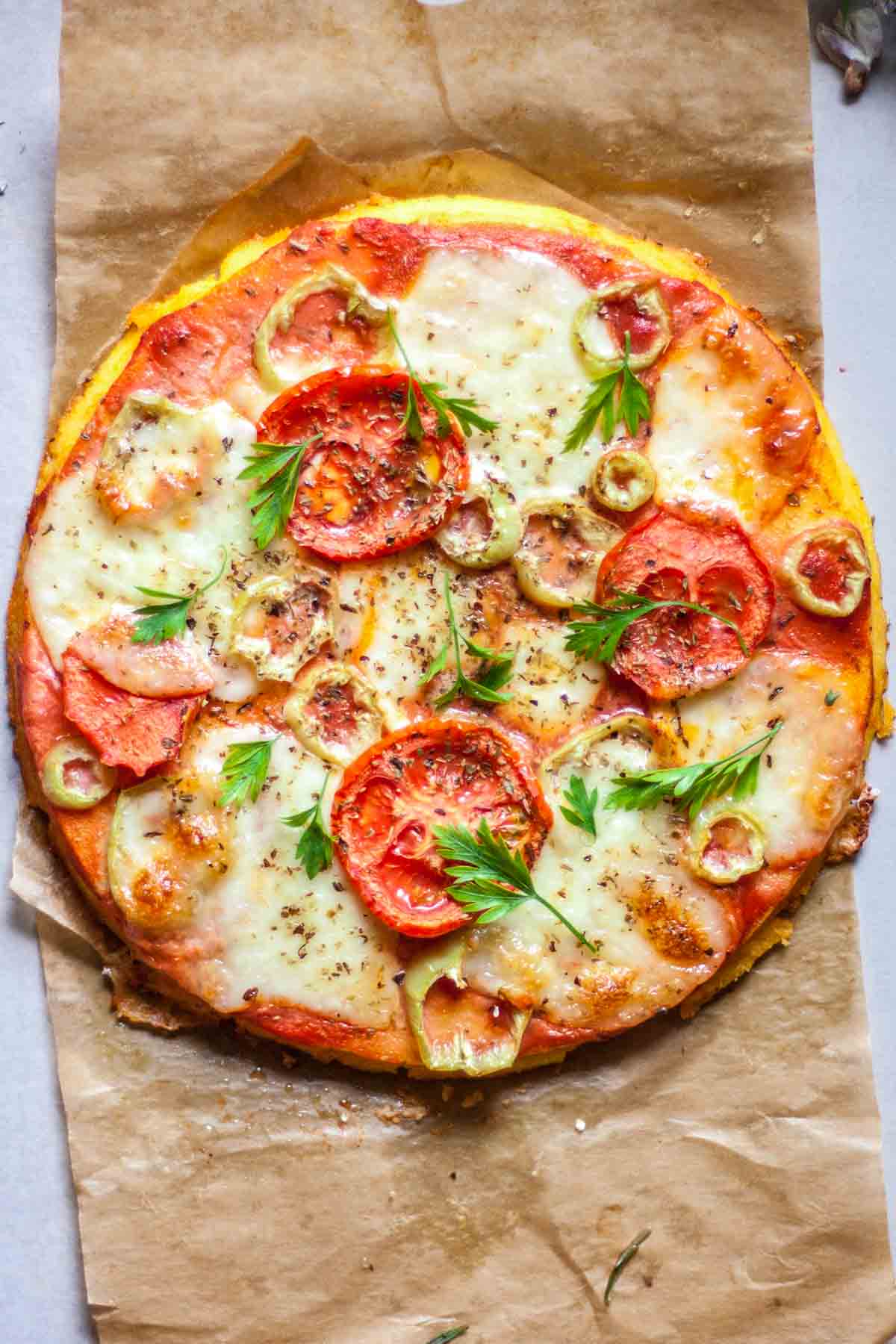 Polenta pizza on a baking paper topped with tomatoes and cheese.