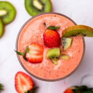 Kiwi and strawberry smoothie in a glass decorated with strawberries and kiwis.