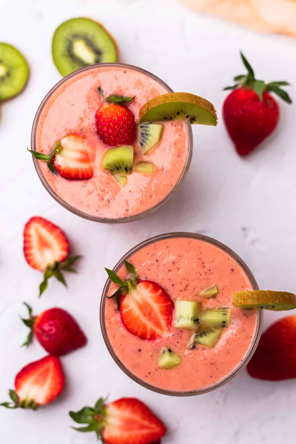 Two Glasses of Kiwi Quencher Tropical Smoothie decorated with strawberries and kiwis