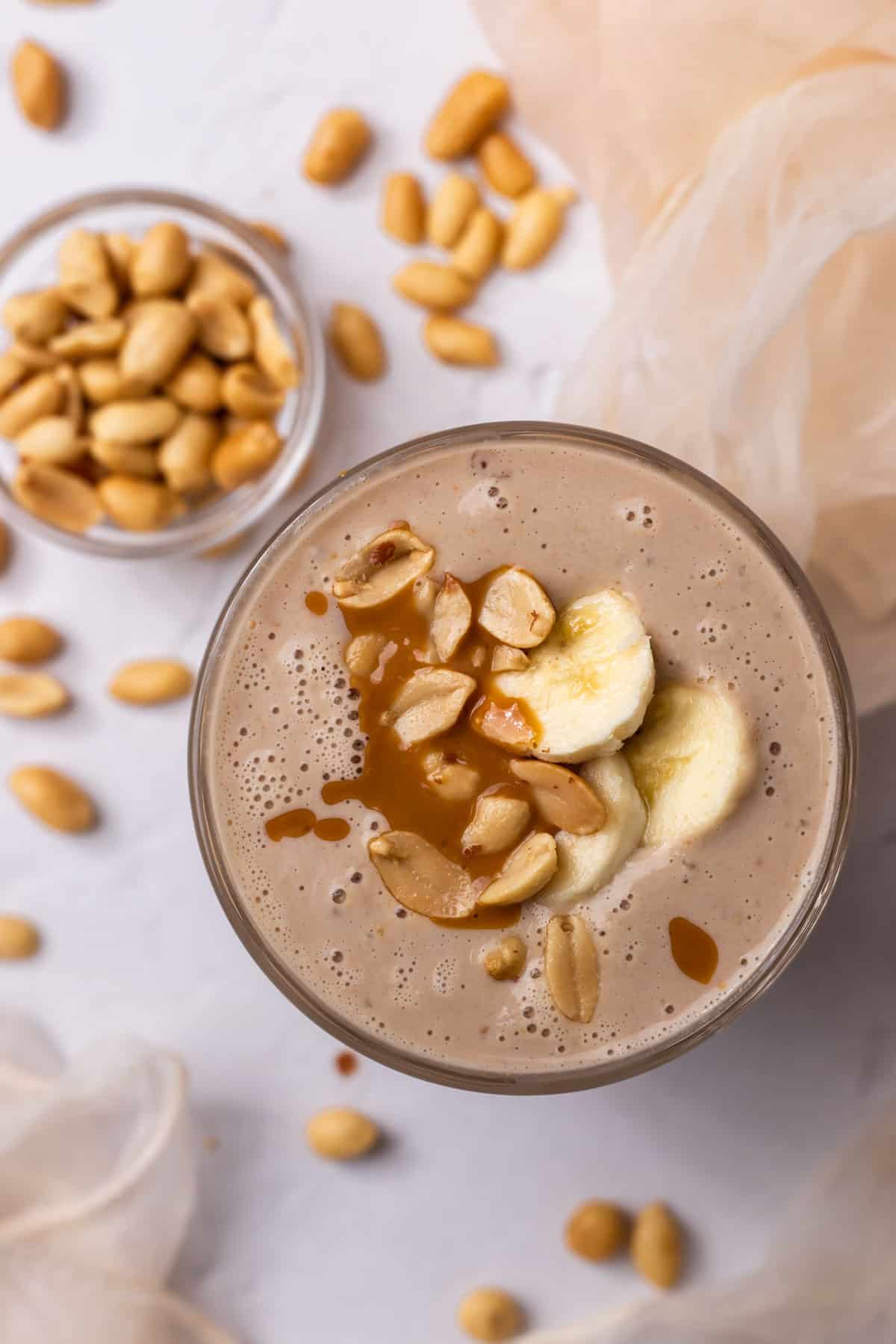 Peanut butter smoothie decorated with banana slices, peanut butter and peanuts