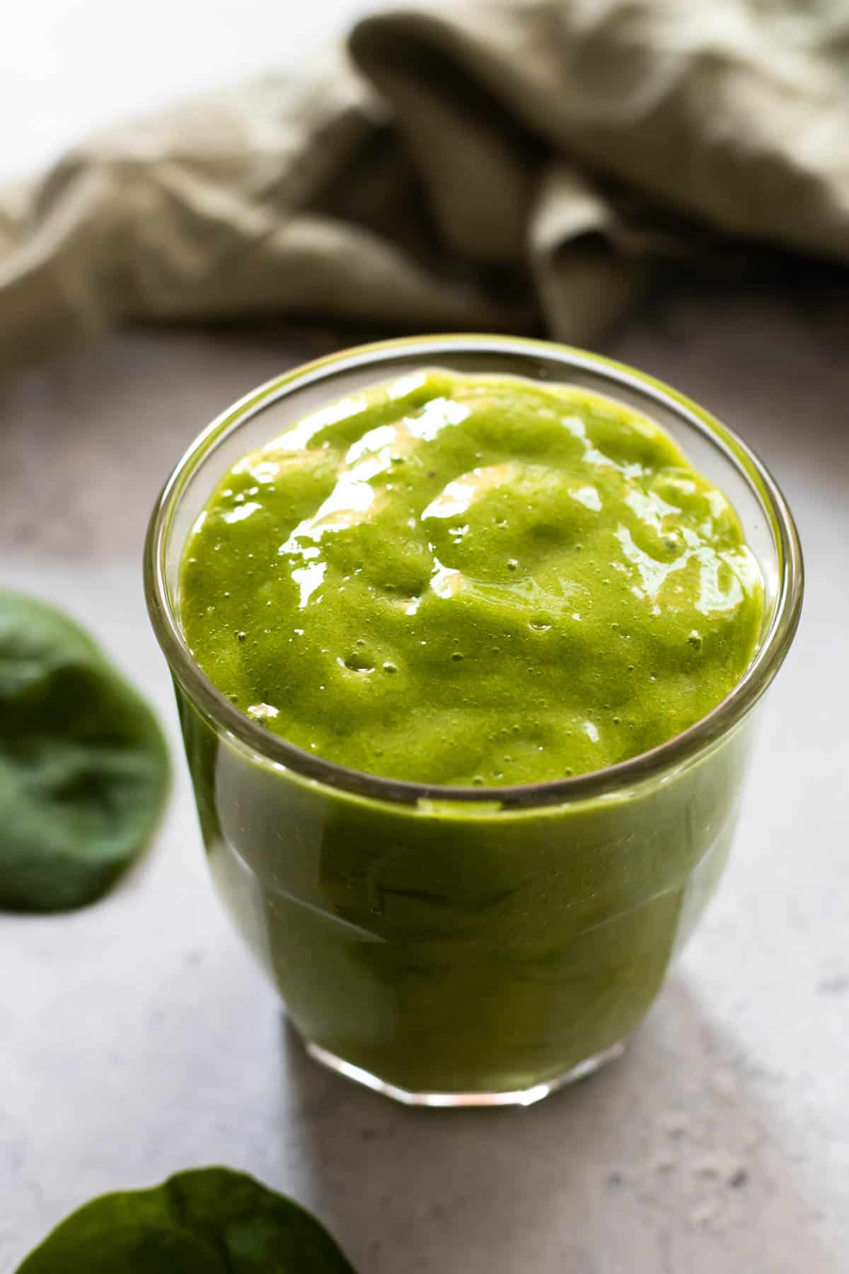 Green Detox Island Green Smoothie in a glass with baby spinach leaves on the side.