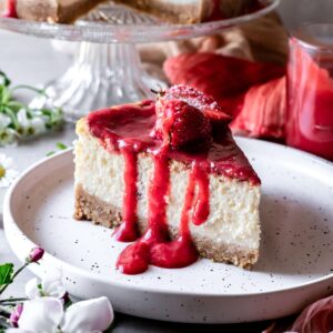 A slice of gluten-free New York style cheesecake with strawberry sauce.