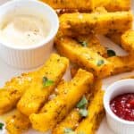 Polenta fries on a plate with mayo and ketchup in small sauce bowls