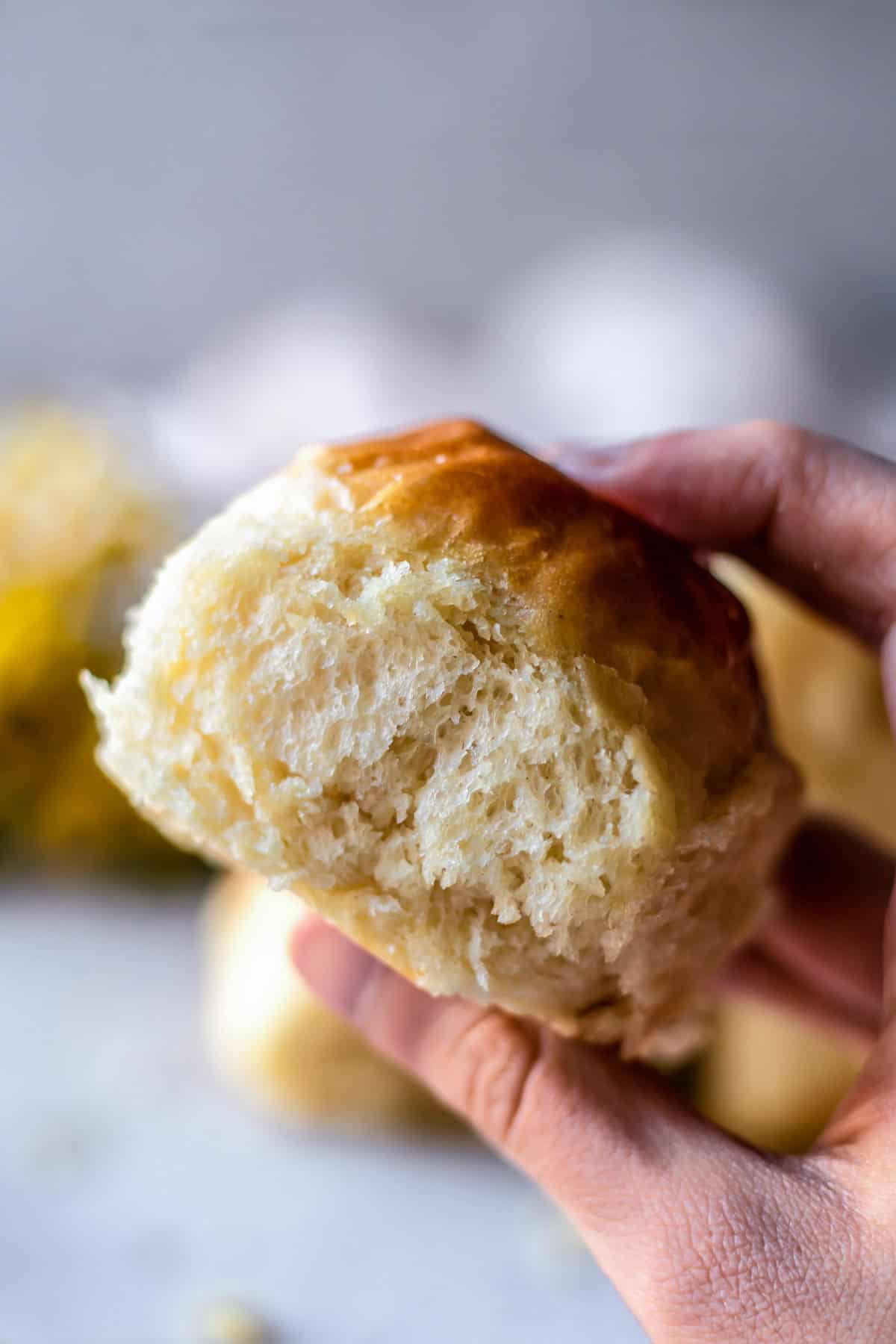 Holding one dinner roll, photographed from the side to see the fluffy texture.