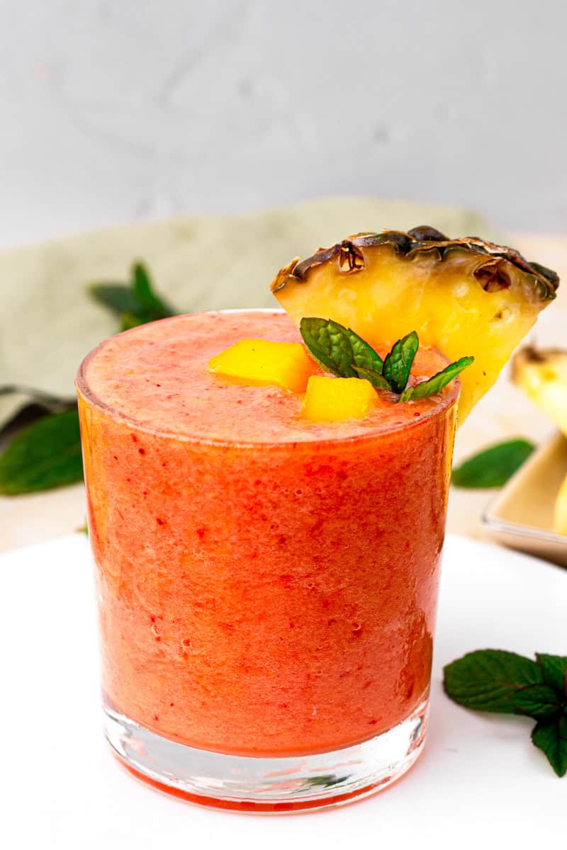 A glass of sunrise sunset smoothie decorated with mango, pineapple and mint.