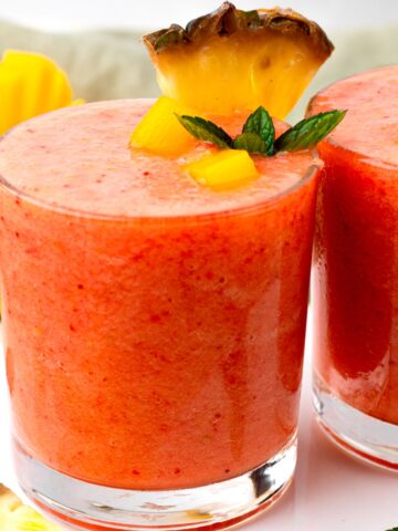 Two glasses of sunrise sunset smoothie decorated with mint and mango.