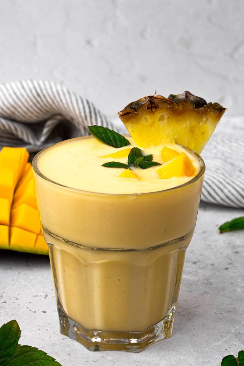 clear glass full of mango smoothie with a chunk of pineapple on the rim of the glass
