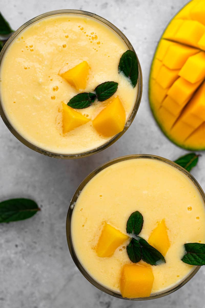 two glasses full of creamy mango smoothie topped with mango chunks