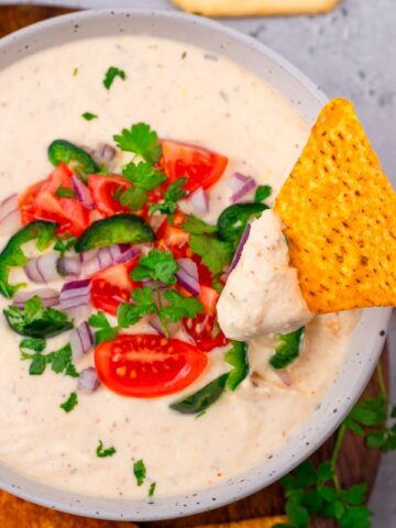 hand dipping a chip into a bowl of cottage cheese queso dip