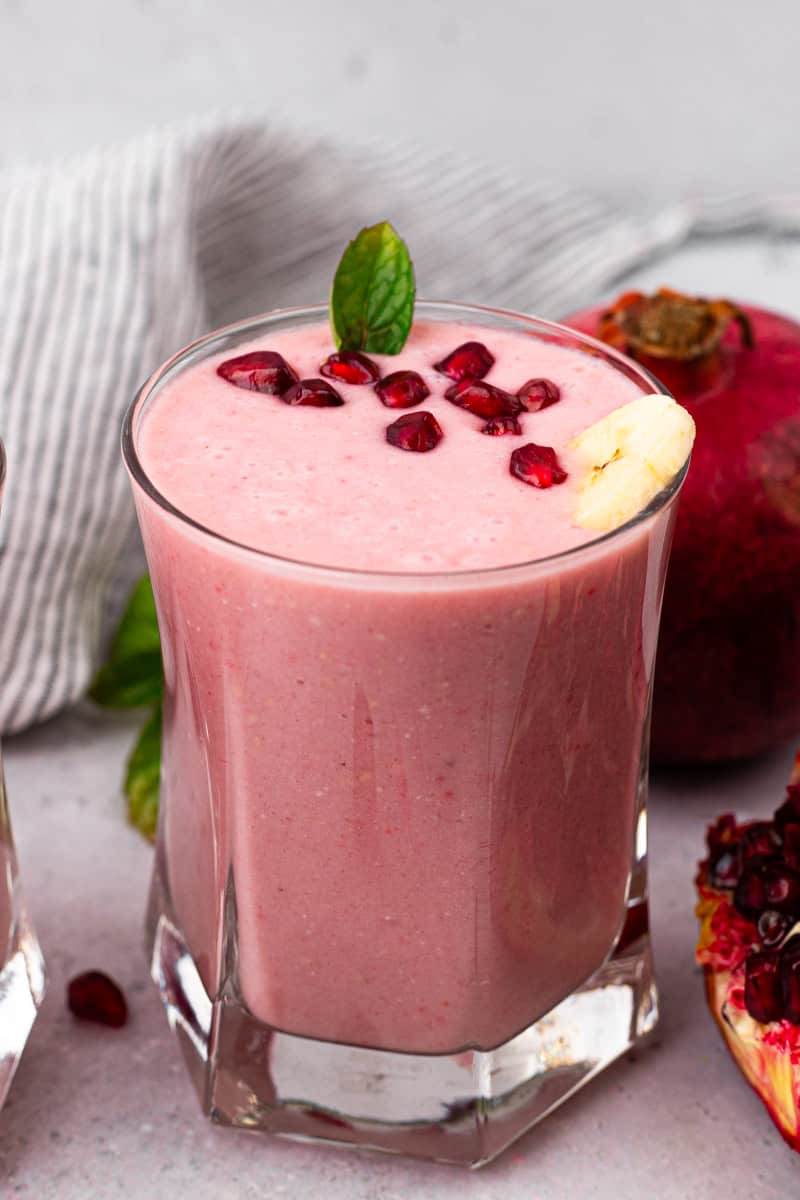 glass full of pomegranate smoothie with pomegranate seeds on top