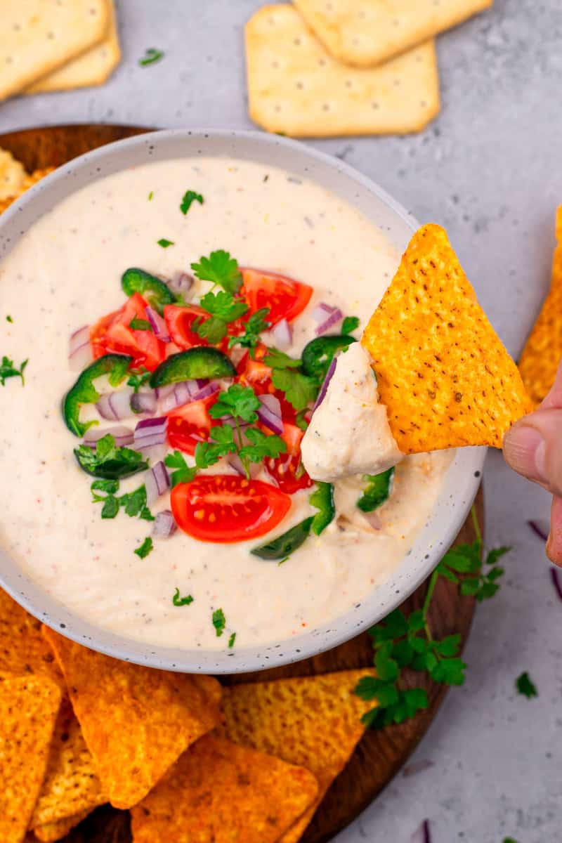 hand dipping a chip into a bowl of cottage cheese queso dip
