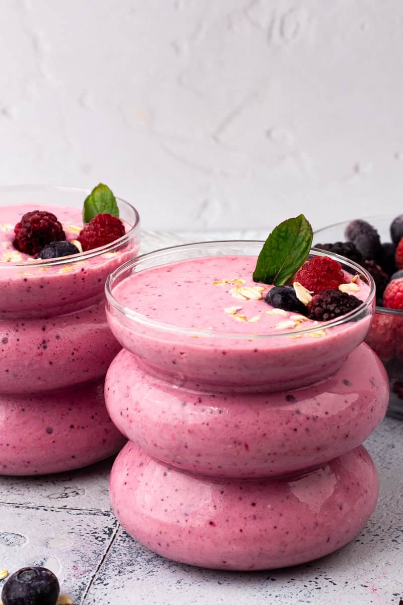 Triple Berry Oat Tropical Smoothie in a glass with fresh berry toppings