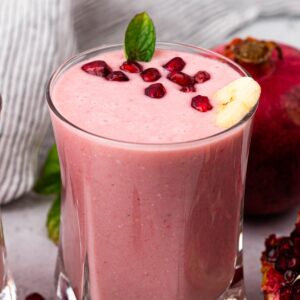 glass full of pomegranate smoothie with pomegranate seeds on top