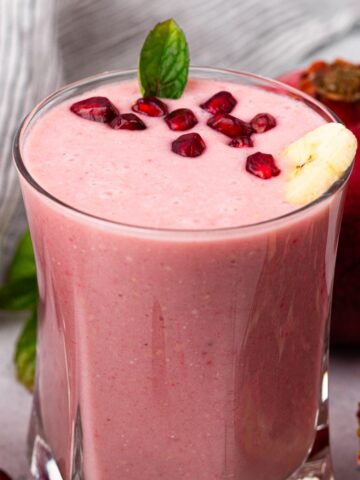 glass full of pomegranate smoothie with pomegranate seeds on top