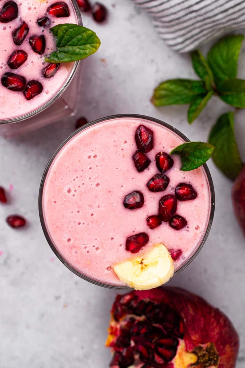 a top down view of a pomegranate smoothie in a glass topped with pomegranate seeds